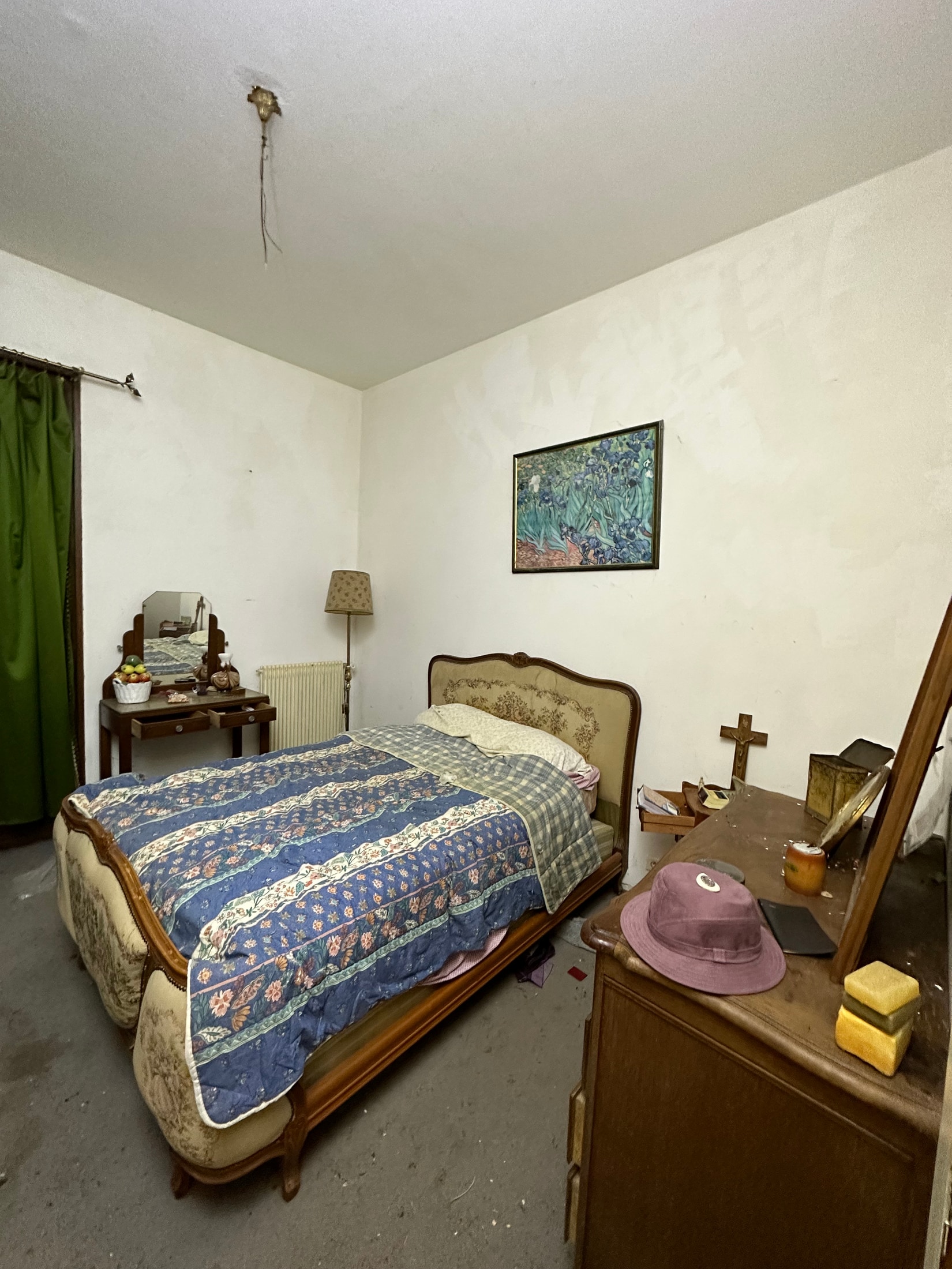 Verlassenes Schlafzimmer mit altem Bett, Nachttisch und zurückgelassenen Dingen